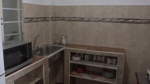 A compact kitchen with a microwave, sink, and shelves for dishes and utensils. - Guest House Yuraq Wasi (Cusco)
