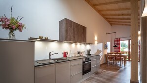 A modern kitchen with a wooden ceiling, a dining area with red chairs, and a view of the outdoors. - Apartment Wildbarren, 55sqm, balcony (Oberaudorf)