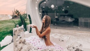 A woman sitting in a natural rock formation with a modern building in the background. - The Cloud Unique Beachfront Villa (Tabanan)