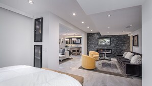 Ein modernes Schlafzimmer mit einem großen Bett, einem Essbereich mit Küche im Hintergrund und einem Wohnzimmer mit Kamin.