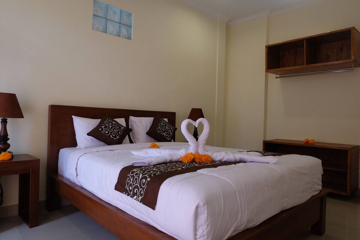 A neatly made bed with a heart-shaped towel arrangement, a wooden headboard, and a bedside table with a lamp.