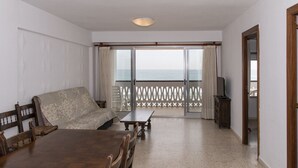 Ett rum med ett matbord i trä, en soffa, en tv och en balkong med utsikt över havet.