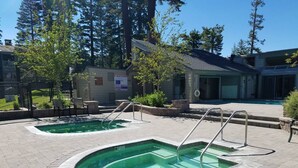 A pool area with two separate pools, each with a metal ladder. There are lounge chairs and a building with a sign in the background. - Retreat at Canyon Lodge w/ Mountain Views! (Mammoth Lakes)