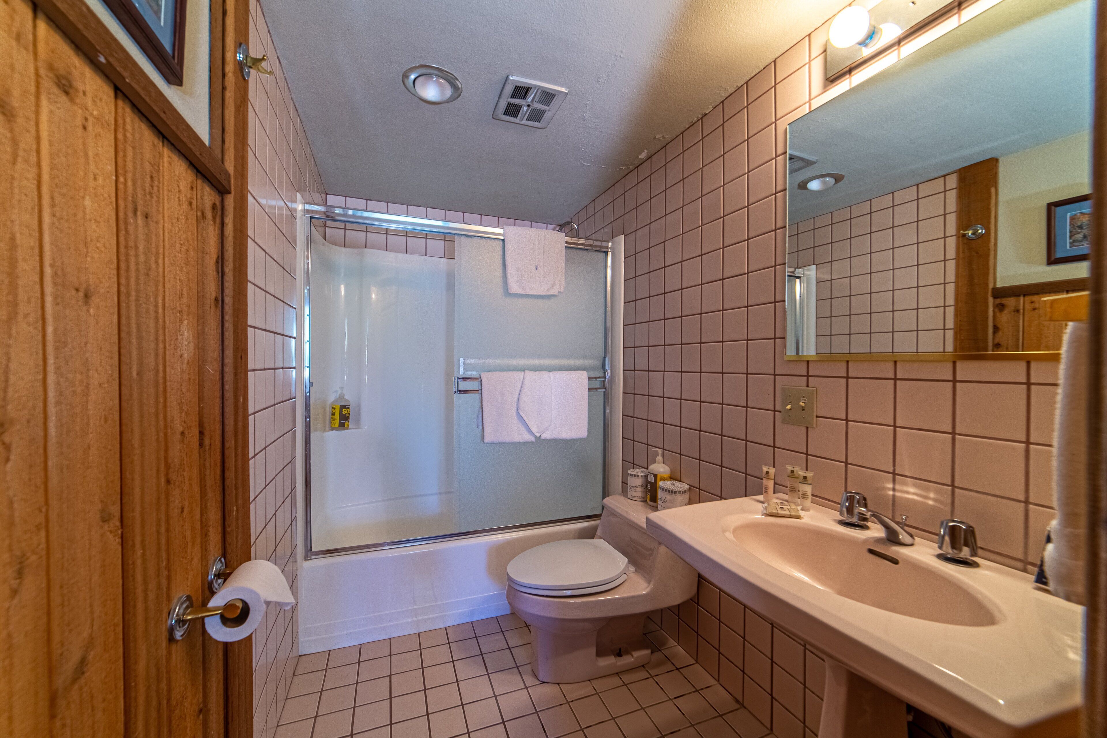 A bathroom with a shower, toilet, sink, and mirror.