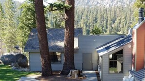 A building with a patio area featuring picnic tables and a stone fire pit, surrounded by large trees and a mountainous backdrop. - Retreat at Canyon Lodge w/ Mountain Views! (Mammoth Lakes)