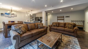 A modern living room with two brown leather sofas, a wooden coffee table, and a dining area with a wooden table and chairs.