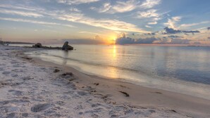 Una playa con mar tranquilo, una puesta de sol y huellas en la arena.