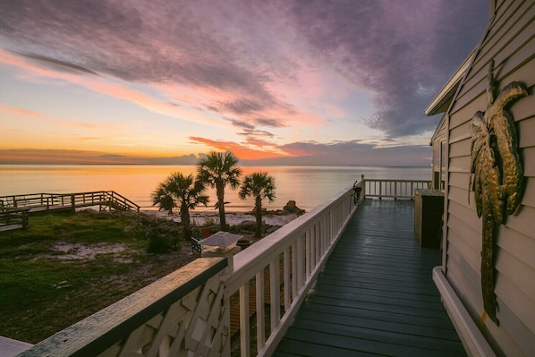 A wooden deck leading to a beach with palm trees and a sunset view.