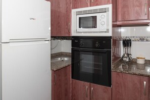 Eine Küche mit einem weißen Kühlschrank, einer weißen Mikrowelle und einem schwarzen Backofen.