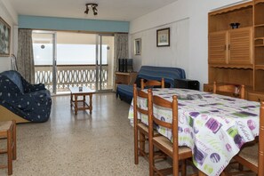 Ein Zimmer mit Esstisch, Holzsesseln, einer Couch, einem Fernseher und einem Balkon mit Blick.