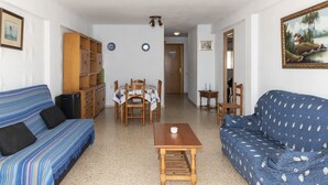 A living room with a blue sofa, a wooden table, and a dining table with chairs. There is a bookshelf and a painting on the wall. - LIDER, 10-B (Cullera)