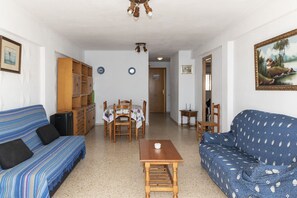 A living room with a blue sofa, a wooden table, and a dining table with chairs. There is a bookshelf and a painting on the wall. - LIDER, 10-B (Cullera)