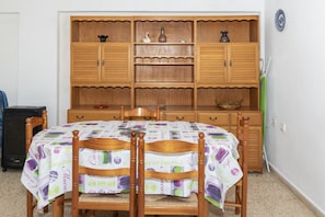 A dining area with a wooden table and chairs, a patterned tablecloth, and a wooden cabinet with shelves.