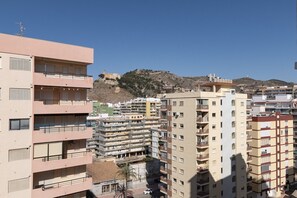 A multi-story residential building with balconies, a clear sky, and a hilly landscape in the background.