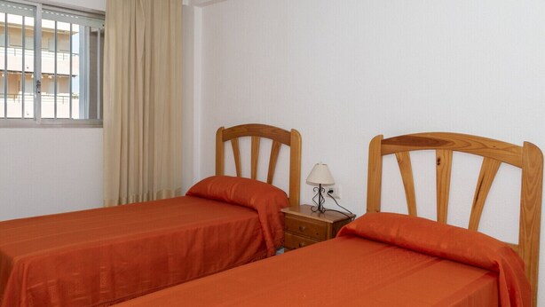 A room with two single beds, a nightstand with a lamp, and a window with curtains. - LIDER, 10-B (Cullera)