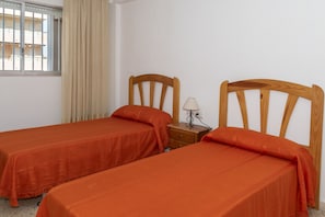 Ein Zimmer mit zwei Einzelbetten, einem Nachttisch mit Lampe und einem Fenster mit Vorhängen.