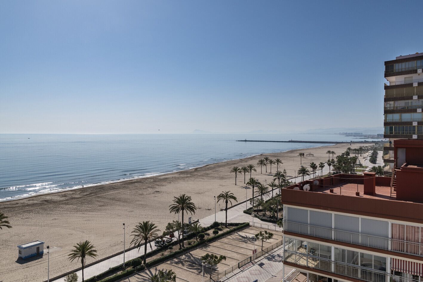 A beachfront hotel with a view of the ocean and a distant pier.