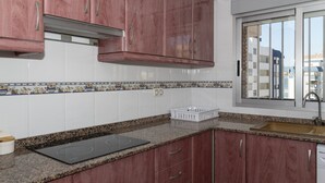 A kitchen with granite countertops, a black induction cooktop, wooden cabinets, and a window with a city view. - LIDER, 10-B (Cullera)
