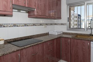 A kitchen with granite countertops, a black induction cooktop, wooden cabinets, and a window with a city view. - LIDER, 10-B (Cullera)