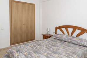 Ein Schlafzimmer mit Holzschrank, Nachttisch mit Lampe und Bett mit gemustertem Überwurf.