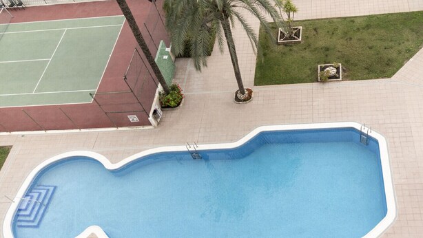 An outdoor swimming pool with a wavy edge, surrounded by a tiled deck and small planters with flowers. - LIDER, 10-B (Cullera)