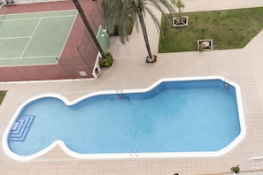 An outdoor swimming pool with a wavy edge, surrounded by a tiled deck and small planters with flowers.