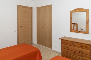 A bedroom with two wooden wardrobes, a dresser, and a mirror on the wall.