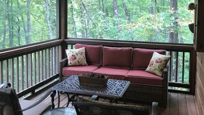 A wooden deck with a cushioned bench and a table, overlooking a forest. - Peaceful Mountain Cabin (Sapphire)