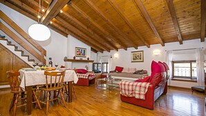 A spacious living area with wooden flooring, a dining table set for a meal, and a cozy seating arrangement with red sofas and a couch. - Residenza Rocca del Lago 2, Riva del Garda, Italy (Riva del Garda)