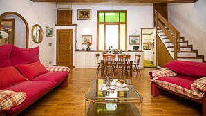 A cozy living room with two red sofas, a glass coffee table, wooden flooring, a kitchen area with a dining table, and a staircase. - Residenza Rocca del Lago 2, Riva del Garda, Italy (Riva del Garda)