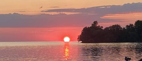A sunset over a calm body of water with a dock and trees in the foreground.