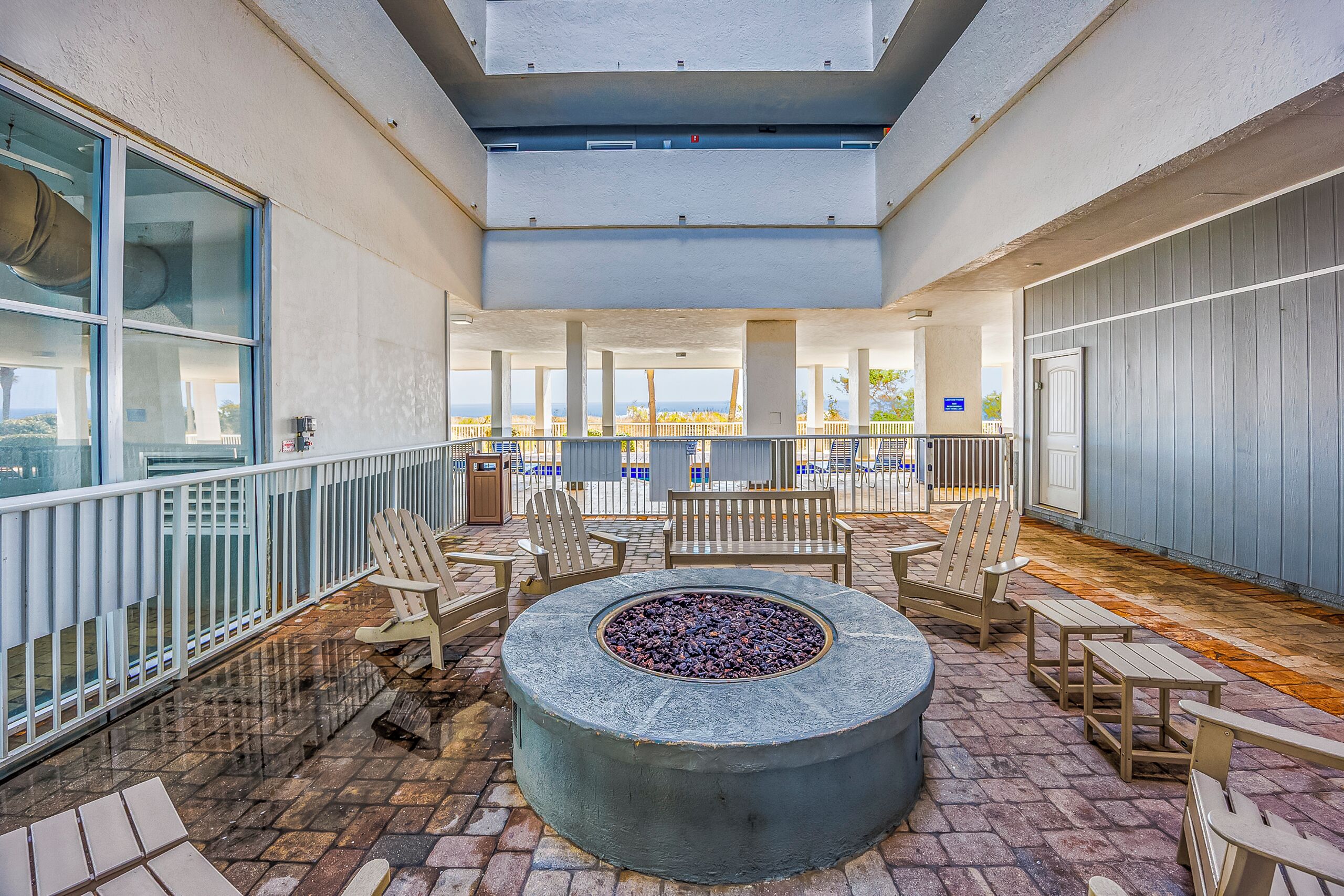 A covered outdoor seating area with a fire pit, wooden chairs, and tables, overlooking a scenic view.