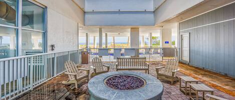 A covered outdoor seating area with a fire pit, wooden chairs, and tables, overlooking a scenic view.