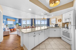 A modern kitchen with a large island, white cabinetry, and a view of the ocean.