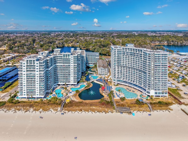 A high-rise hotel with multiple balconies, a central pool area, and a beach view.
