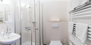 Uma casa de banho moderna com cabine de duche em vidro, lavatório branco e suporte para toalhas.