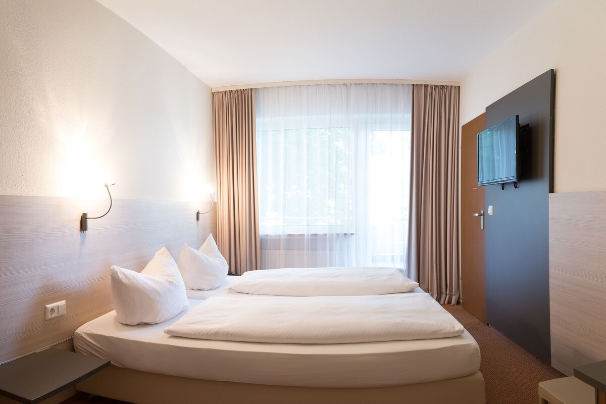 Quarto de hotel com uma cama, televisão e secretária.