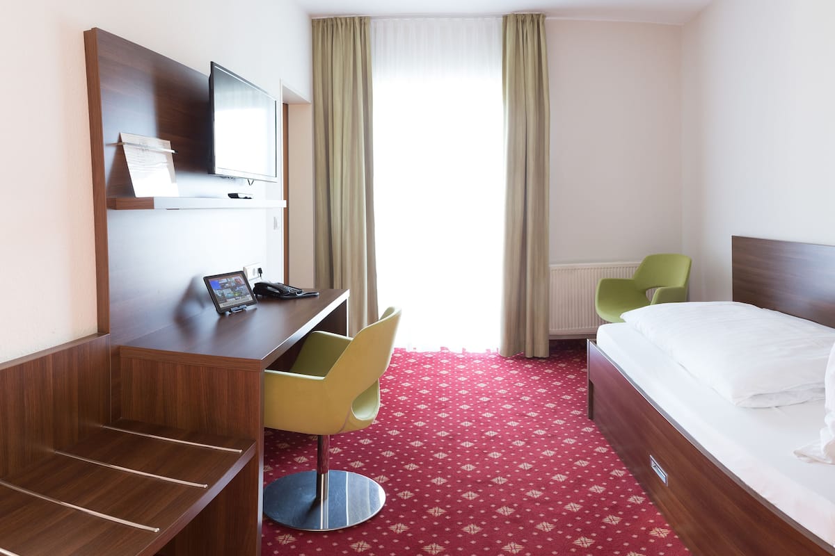 Quarto de hotel com escrivaninha, cadeira, cama e televisão fixada na parede.