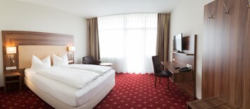 Ein Hotelzimmer mit einem großen Bett, einem Schreibtisch, einem Sessel, einem Fernseher und einem Kleiderschrank.