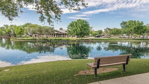 Un parc avec un étang, un banc et un bâtiment en arrière-plan.