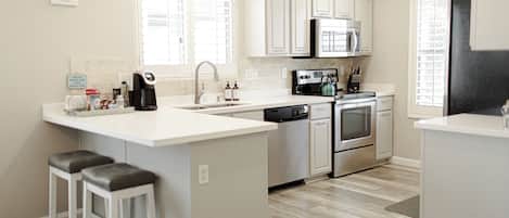 A modern kitchen with white cabinetry, stainless steel appliances, and a central island with stools.