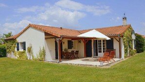Ein Haus mit Ziegeldach, einer überdachten Terrasse mit Gartenmöbeln und einem Rasen.
