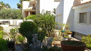 A courtyard with potted plants, a stone bench, and a white building with a tiled roof. - Villa Los Balconess,<br>Is available from  6 nights (Torrevieja)