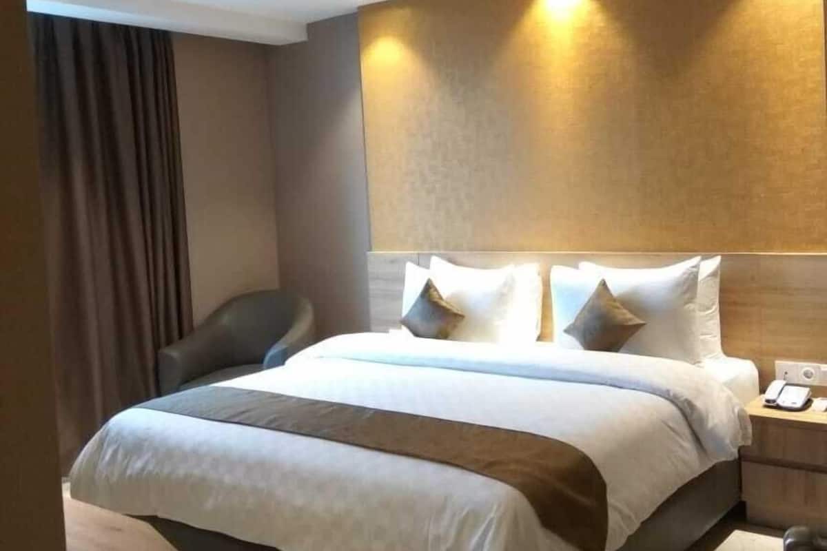 Moderni hotellihuone, jossa on suuri sänky, yöpöytä ja sängynpääty, jossa on sisäänrakennettu valaistus.