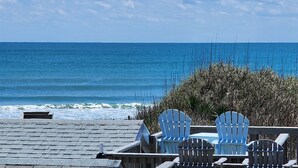 A seaside view with a wooden deck, two Adirondack chairs, and a view of the ocean.