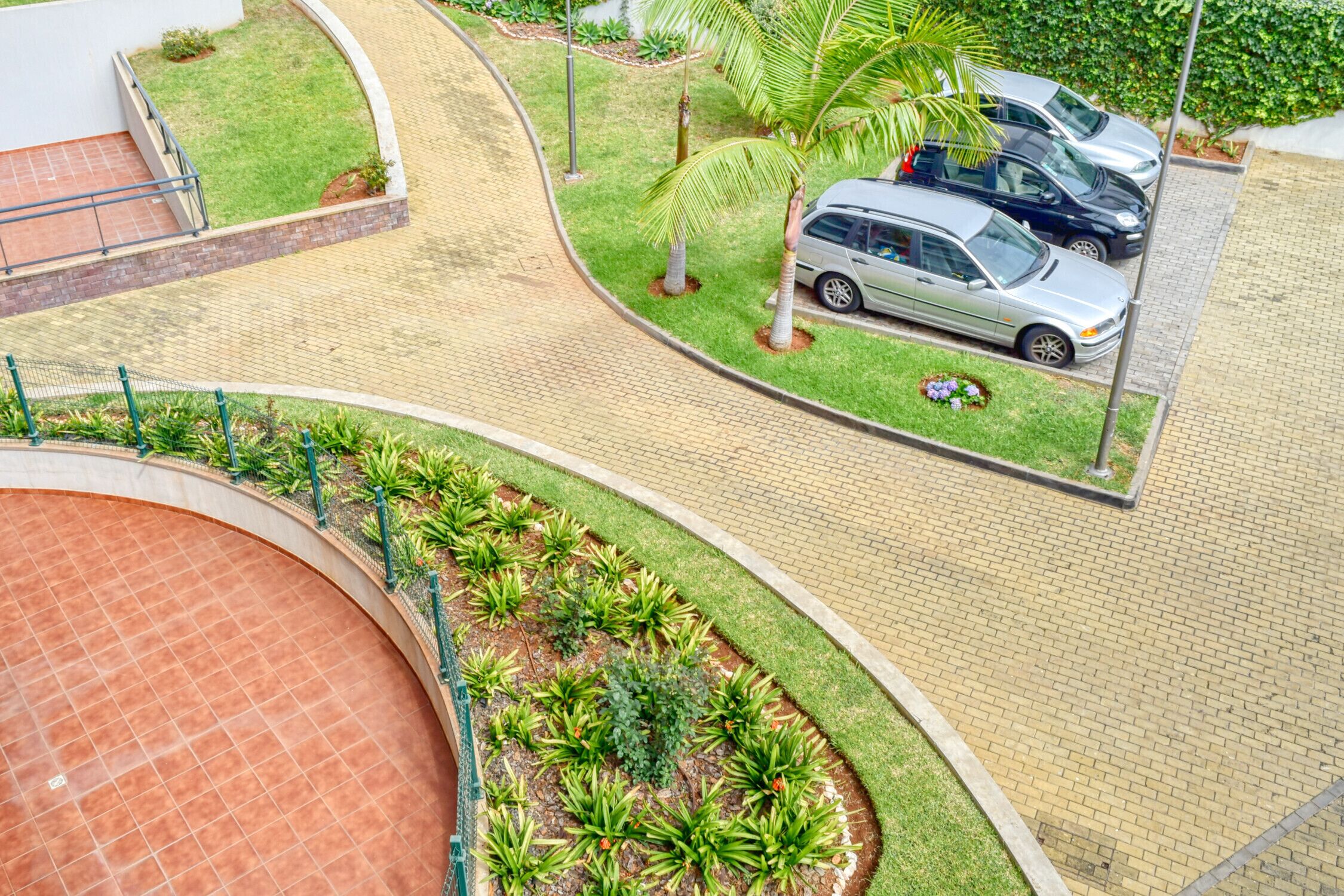 A parking area with cars, a curved pathway, and a landscaped garden with small trees and shrubs.