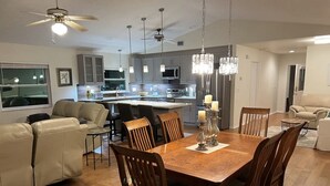 A modern kitchen with a central island, pendant lighting, and a dining area with a wooden table and chairs.