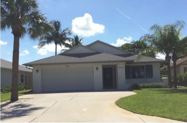 A single-story house with a garage, surrounded by palm trees and a clear sky.