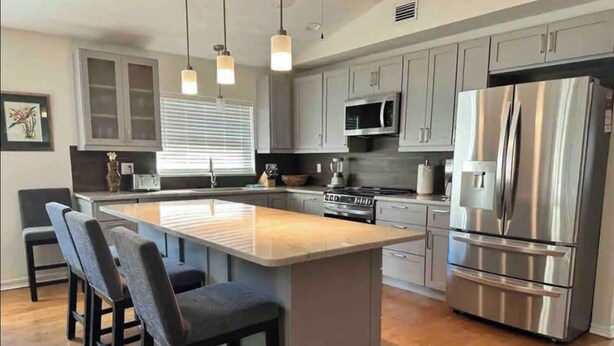 A modern kitchen with grey cabinets, stainless steel appliances, and a central island with bar stools.