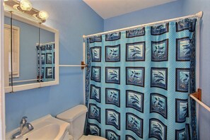 A bathroom with a blue shower curtain featuring dolphin patterns, a white sink, and a mirror above the sink. - Beach Escape is a cool and calm get-a-way! (HATTERAS)